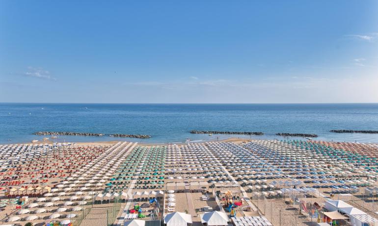 Überfüllter Strand mit bunten Sonnenschirmen und ruhigem Meer.