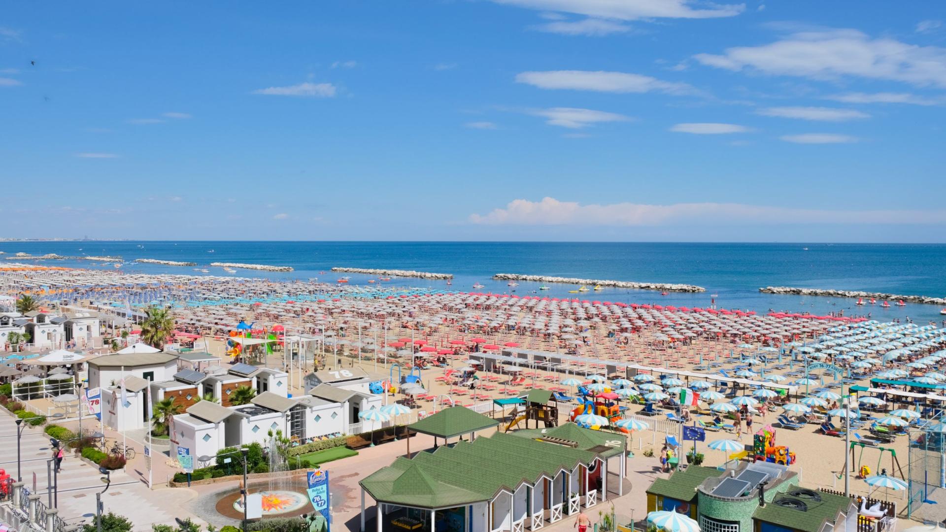 Überfüllter Strand mit bunten Sonnenschirmen und ruhigem Meer.