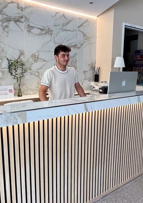Rezeptionist steht hinter einem modernen Schreibtisch mit Laptop.